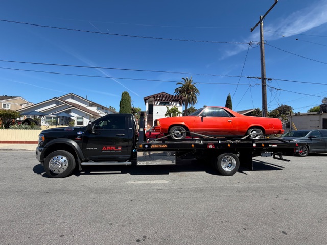 Apple Roadside Assistance flatbed tow truck transporting a classic red El Camino in Los Angeles